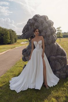 a woman standing in front of a statue wearing a white dress with high slits