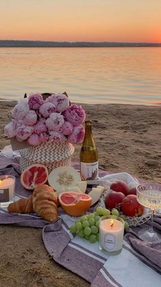 a picnic on the beach with wine, fruit and bread in front of water at sunset