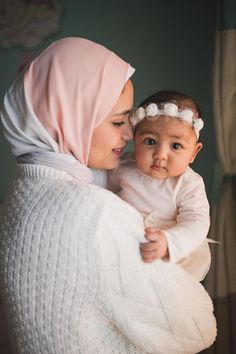 a woman holding a baby while wearing a white sweater and headband with flowers on it