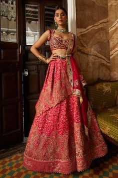 a woman in a red and gold bridal gown standing next to a door with her hands on her hips