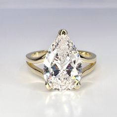 a pear shaped diamond ring on a white surface with the center stone in yellow gold