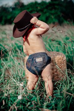 a baby wearing a cowboy hat is sitting in the grass