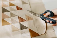 someone using scissors to cut fabric on a piece of paper that has triangles in it