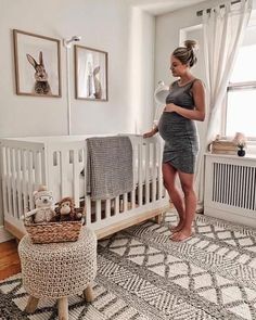 a woman standing next to a white crib in a room with pictures on the wall