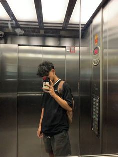 a man standing in front of an elevator taking a selfie with his cell phone