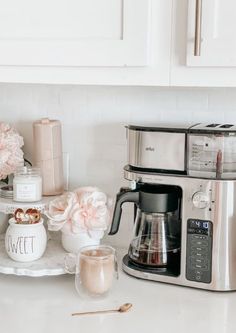 the coffee maker is sitting on the counter next to some cups and spoons with flowers in them