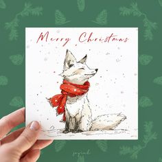 a hand holding up a christmas card with a white dog wearing a red scarf