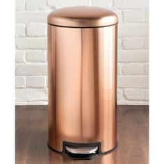 a large metal trash can sitting on top of a wooden floor next to a brick wall