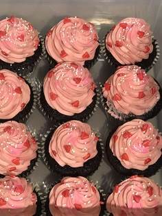 twelve cupcakes with pink frosting and hearts on them in a plastic box