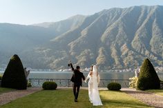 a bride and groom are walking towards the water with mountains in the backgroud