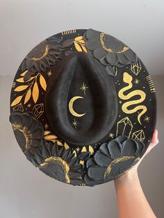 Halloween hat Brim is about 3.75" wide  Content: Vegan Suede Adjustable to fit your head better if needed  Elevate your style with this stunning hand-painted wide-brim fedora, crafted from luxurious vegan suede in a timeless black and gold palette. This one-of-a-kind piece is adorned with intricate designs featuring a serpent winding gracefully around the crown, sparkling crystals, celestial stars, delicate leaves, and a crescent moon. Each flower is meticulously painted with thick, textured strokes, adding a unique tactile dimension to the hat's sophisticated design. This fedora isn't just a hat; it's a wearable work of art. Perfect for making a statement at festivals, special events, or just adding a touch of magic to your everyday outfits. Whether you're dressing up or down, this versat Adjustable Flat Brim Halloween Hat, Adjustable Flat Brim Hat For Halloween, Adjustable Flat Brim Halloween Costume Hat, Black Brimmed Fedora For Halloween, Handmade Black High Crown Top Hat, Black Curved Brim Fedora For Halloween, Halloween Adjustable Wide Brim Top Hat, Halloween Wide Brim Top Hat, Adjustable Brimmed Felt Hat For Halloween