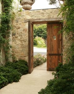 an open wooden door leading to a lush green garden with stone walls and greenery