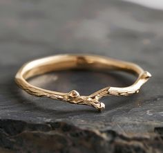 a close up of a gold ring on top of a black stone slab with a tree branch in the middle