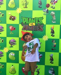 a young boy standing in front of a green wall with plants and zombies on it