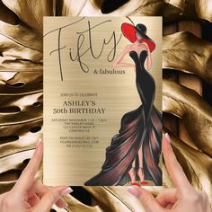 a woman in a black dress holding up a 50th birthday card with the words fifty and fabulous on it