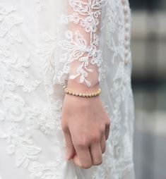 a close up of a person wearing a white dress and holding onto a gold bracelet