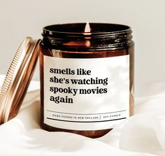 a candle that is sitting on top of a white sheet next to a jar with the words smells like she's watching spooky movies again