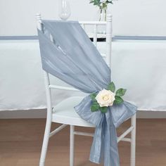 a white chair with a blue sash and flower on it's back, sitting in front of a table