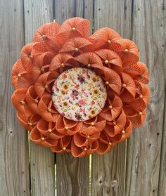 an orange flower is hanging on a wooden fence with other flowers in the center and around it