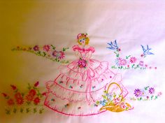 an embroidered piece of cloth with a dress and flowers in the center, on a yellow background