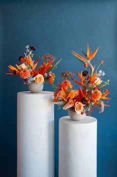 two white vases with orange and red flowers in them sitting on top of each other