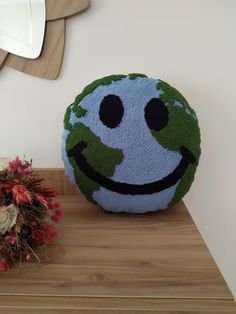 a smiley face pillow sitting on top of a wooden table next to a vase with flowers