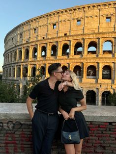 a man and woman kissing in front of the colossion