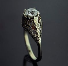 a ring with a diamond in the center on a black surface and an intricate design around it