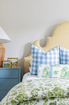 a bed with green and blue pillows on it's headboard next to a night stand