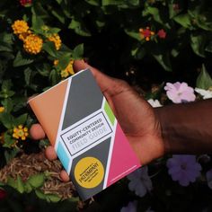 a person holding up a box with different colored papers in front of some colorful flowers