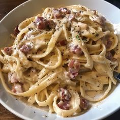 a white bowl filled with pasta covered in sauce and meats next to a fork