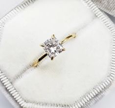 an engagement ring with a single diamond in it sitting on a white velvet case,