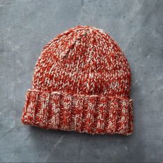 an orange and white knitted beanie sitting on top of a gray surface next to a pair of scissors