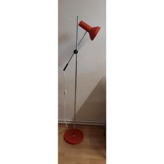 a red floor lamp sitting on top of a wooden floor next to a white wall