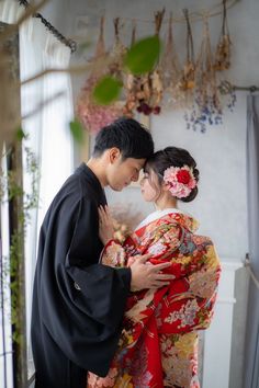 a man and woman dressed in traditional japanese garb embracing each other with flowers on their hair