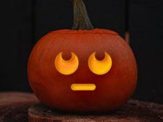 a carved pumpkin with glowing eyes on it's face and nose, sitting on a piece of wood