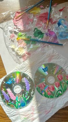 two cds sitting on top of a table covered in plastic wrap and paintbrushes