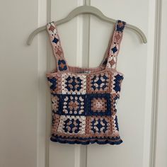 a pink and blue crocheted top hanging on a white door hanger next to a wooden door