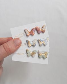 a person is holding four different colored butterfly magnets in their left hand and the other one has gold, silver, and pink