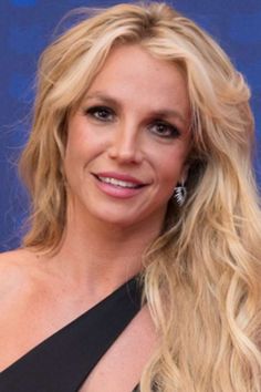 a woman with long blonde hair wearing a black dress and diamond earrings on her left ear