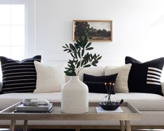 a living room with white couches and black pillows on the coffee table in front of it