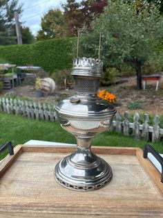 a metal candle holder sitting on top of a wooden tray in front of a garden