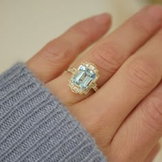 a woman's hand wearing a ring with an aqua blue topazte surrounded by diamonds