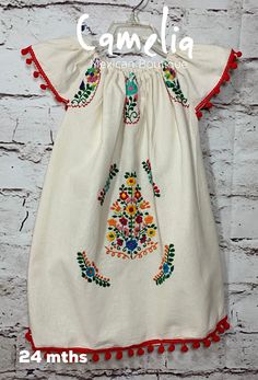 Precious Mexican dress for girls with fun colorful poms around dropped shoulder sleeve and hem line. Dress has fine thread frontal embroidery. Color selection is based on pom-pom color. Please note that embroidery pattern and thread colors may not be identical as pictured. Made with 100% raw cotton (manta). COLOR AND SIZE AVAILABILITY VARY. BE SURE TO SELECT COLOR OPTIONS FOR THE SIZE NEEDED. SIZE WIDTH LENGTH 6MTH 13 13 1 YR 14 15 2 T 18 19 4 T 18 22 6 YR 20 25 8 YR 20 26 10 YR 21 28 Measuremen Festive Cotton Dress With Embroidered Sleeves, Traditional White Dress With Tassels, Traditional Multicolor Dresses With Tassels, Traditional Multicolor Tassel Dress, Girl Mexican, Mexican Babies, Mexican Dress, Baby Bloomers, Mexican Dresses