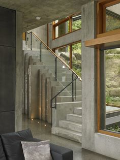 a living room filled with furniture next to a stair case and large glass windows on the wall