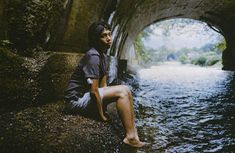 a man sitting on the side of a river under a bridge