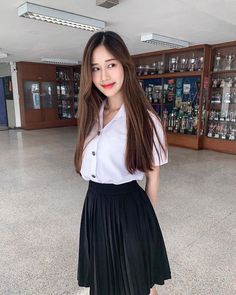 a woman in a white shirt and black pleated skirt posing for the camera with her hands on her hips