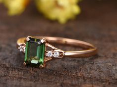 an emerald and diamond ring sitting on top of a piece of wood with flowers in the background