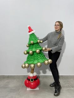 a woman standing next to a christmas tree made out of legos with gold balls