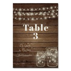 the rustic mason jar wedding table number sign is displayed on a wooden background with string lights